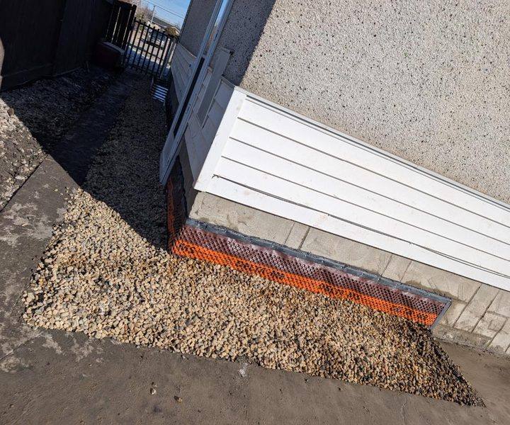 Finished exterior waterproofing with drainage membrane at grade and clean gravel bed along the foundation