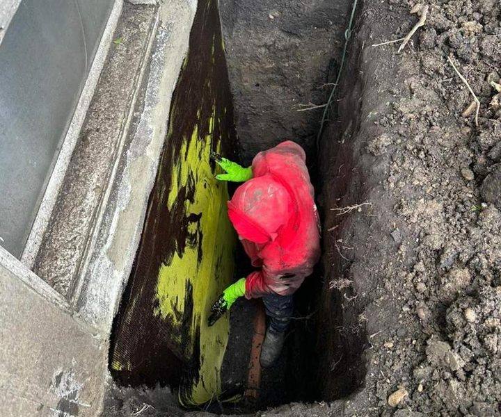 Milad's crew member applying waterproofing membrane in an excavated trench