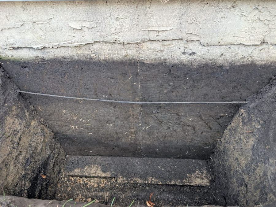 Exposed foundation footing with new weeping tile laid in gravel at the base of a sealed wall