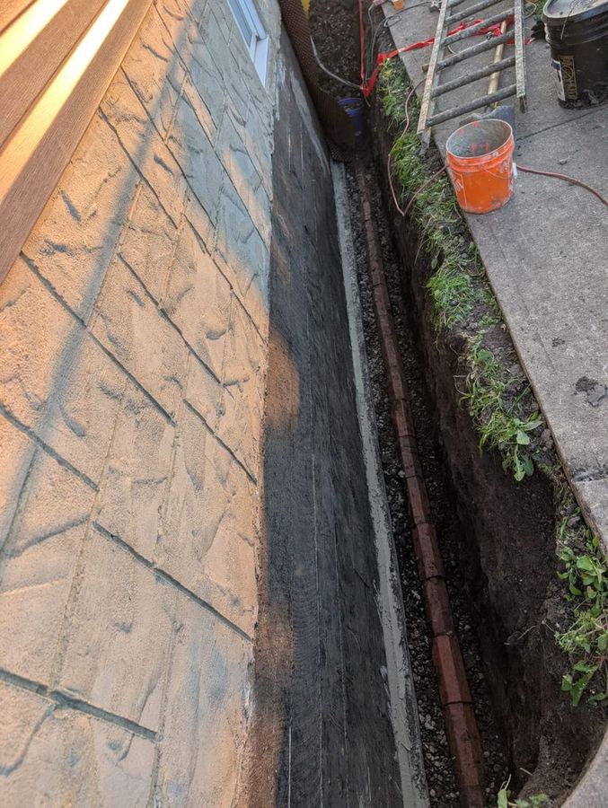 Waterproofed foundation wall with new weeping tile and gravel drainage in an open trench